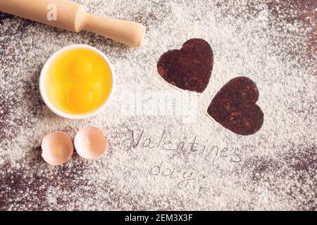 Sprinkled flour with two hearts painted on a wooden background, with a rolling pin and eggs. Baking recipes. Valentine's day concept. Declaration of Stock Photo