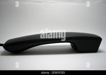 A black telephone receiver from a landline telephone lies on a white background. Stock Photo