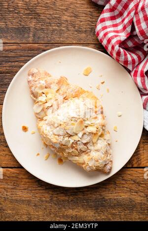 Almond croissant on a plate on old wooden table background, top view Stock Photo