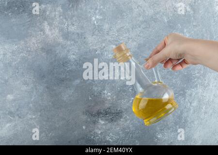 Female hand holding bottle of vegetable oil on grey background Stock Photo