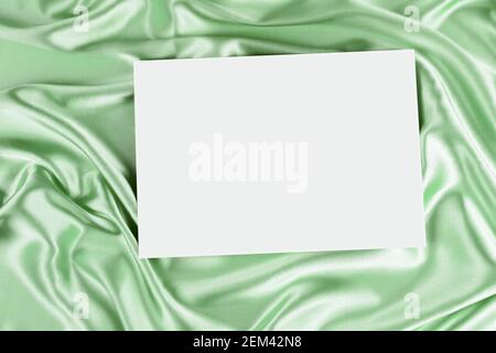 Mock up blank white board canvas poster card for text greeting over draped green color silk cloth background. Top view Stock Photo