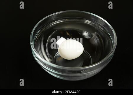 White chicken egg in a glass transparent bowl on a black table close up Stock Photo