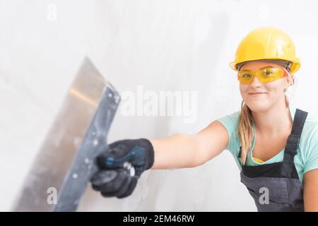 Female molar plasterer worker prepares the wall for applying plaster and leveling surface with spatula. Stock Photo