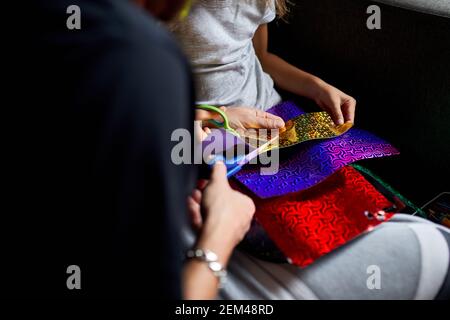 Daughter and father having fun making craft together at home on the sofa, cutting a paper with scissors, dark light, Fathers day, family. Stock Photo