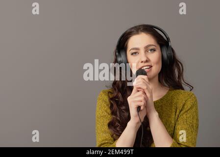 expressive teenager female singing with a microphone and headphones, isolated on gray Stock Photo