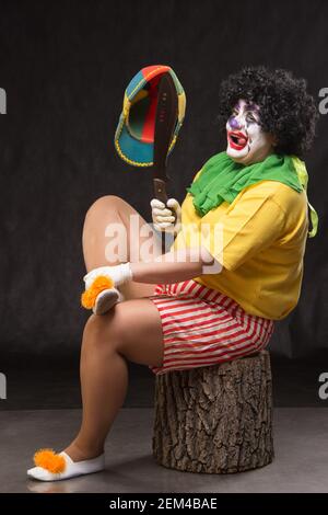 Scary clown with a horrible make-up laughs and with big knives in hands on a black background Stock Photo