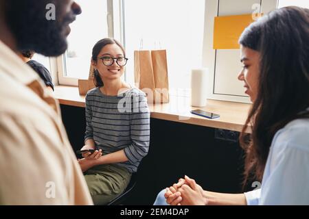 Smiley young woman sitting near window with two friends Stock Photo