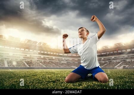 Junior football or soccer player at stadium in flashlight. Young male sportive model training. Moment of win celebrating. Concept of sport, competition, winning, action, motion, overcoming. Stock Photo