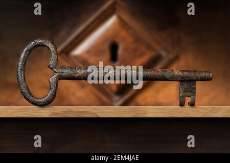Extreme closeup of an old and vintage rusty key on a wooden shelf with a wood keyhole on background. Photography. Stock Photo