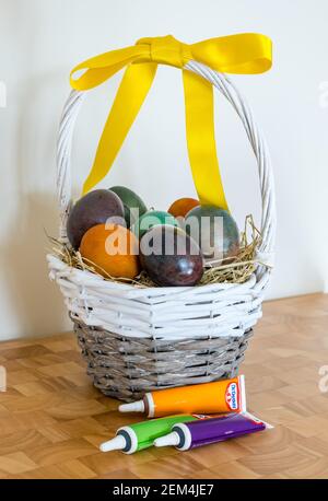 Still life of marbled coloured Easter eggs in willow basket with yellow ribbon and Dr Oetker food colouring Stock Photo