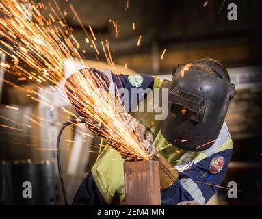 A worker wearing gauntlets and a mask using a grinder on a piece of metal Stock Photo