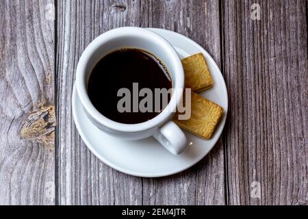 A Black coffee in a cup on a saucer with biscuits on the side laid on a wooden table Stock Photo
