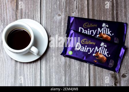 Two Bars of Cadbury Dairy Milk chocolate lad on a wooden table next to a cup of coffee Stock Photo