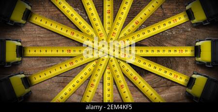 Close-up of a large group of tape measures on a wooden workbench, from above. Photography. Stock Photo