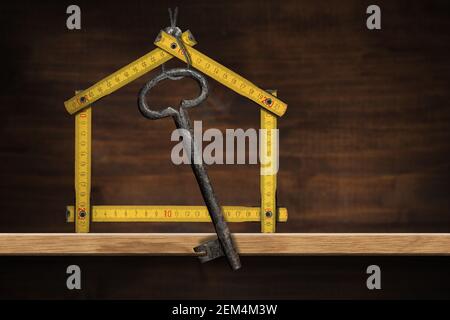 Folding ruler in the shape of a house with an old key hanging. Above a wooden shelf, home interior, Photography. Stock Photo