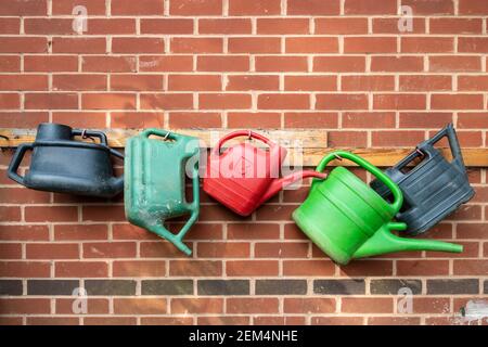 Several colourful watering cans hanging up in a row on a wall Stock Photo