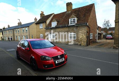 Red Volkswagen Golf Motor car parked in front of historic cottage. Stock Photo