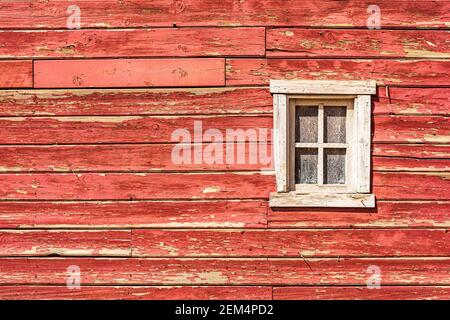 Red barn wall with peeling paint and white frame window. Stock Photo