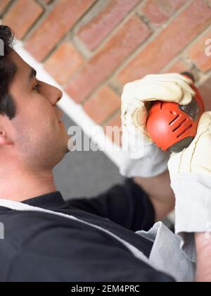 Side profile of a young man using a drill on a wall Stock Photo