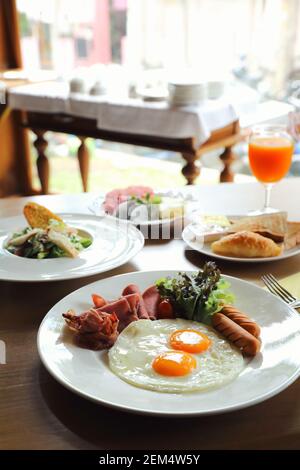 Breakfast set with fried eggs, bacon, sausages, beans, toasts, fresh salad and fruit on wood table Stock Photo