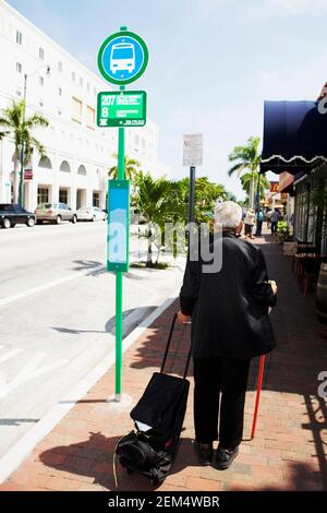 Rear view of a senior man standing at a bus stop with luggage Stock Photo