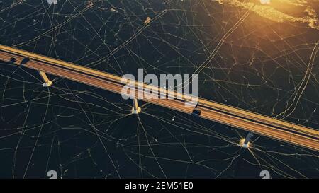 Highway bridge spanning a large body of frozen water covered in thick ice. Stock Photo