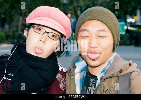 Portrait of a young woman and a young man sticking their tongues out Stock Photo