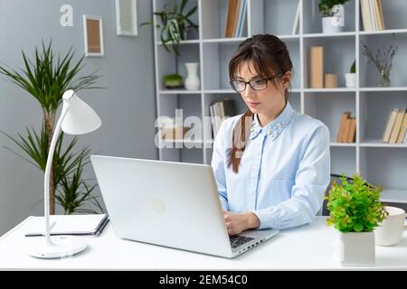 Portrait of a happy young woman freelancer working at home on a laptop. Girl student is studying remotely at home. Stock Photo