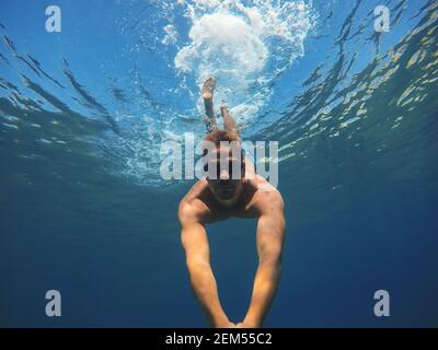 Underwater photo of a young muscular man diving in the turquoise exotic sea and taking a selfie with a stick for summer holidays. Stock Photo