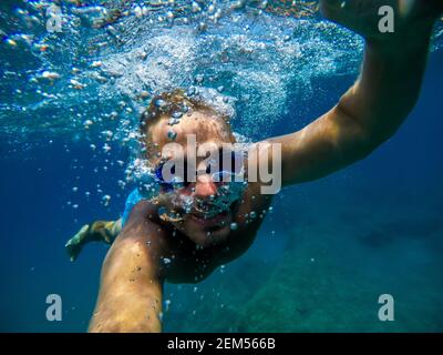 Underwater view of a young diver man swimming and enjoying at the sea for summer vacation while taking a selfie. Stock Photo