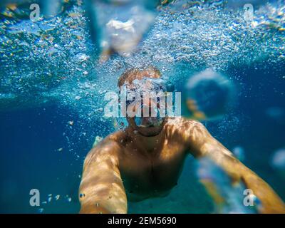 Underwater view of a young playful man relaxing and snorkelling at the sea for summer holidays while taking a selfie. Stock Photo