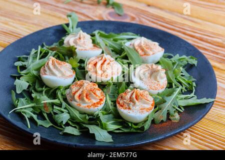 Keto deviled eggs with creamy filling and smoked paprika served with fresh arugula salad, appetizer or finger food, Easter dinner table, close up Stock Photo