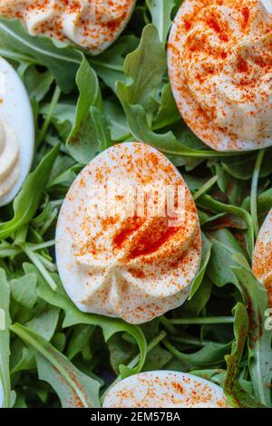 Keto deviled eggs with creamy filling and smoked paprika served with fresh arugula salad, appetizer or finger food, Easter dinner table, close up, dir Stock Photo