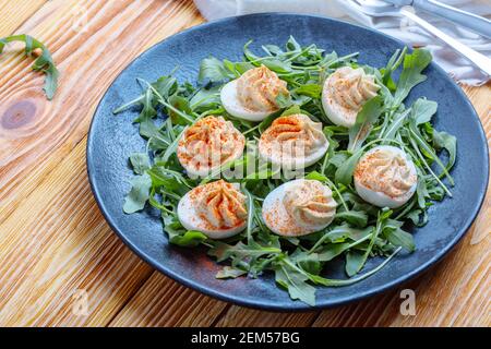 Keto deviled eggs with creamy filling and smoked paprika served with fresh arugula salad, appetizer or finger food, Easter dinner table, close up Stock Photo
