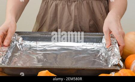 Woman hands placing aluminum foil on baking pan. Baking pumpkin, step by step pumpkin puree recipe, lifestyle Stock Photo
