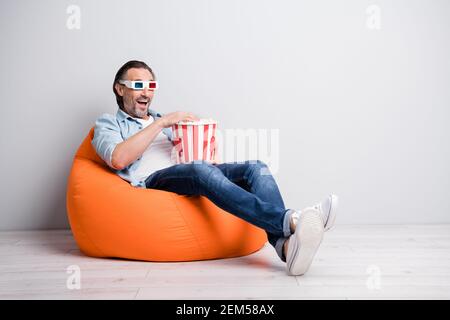 Full length photo of handsome man sit chair wear 3d glasses eat popcorn watch film isolated over grey color background Stock Photo