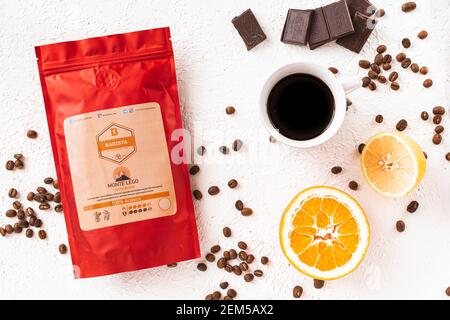 Tiraspol, Moldova - February 12, 2021: red coffee bag with degassing valve, cup of coffee, coffee beans, orange, lemon and chocolate, top view. 100% A Stock Photo