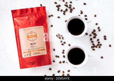 Tiraspol, Moldova - February 12, 2021: red coffee bag with degassing valve, two cups of brewed coffee, coffee grains on a white background, top view. Stock Photo