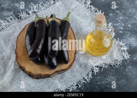Fresh purple eggplant on wooden board and bottle of oil. Top view Stock Photo