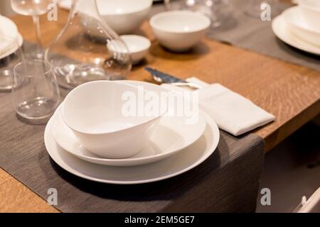 Table with plates and glasses before a party.Piles of white ceramic tableware, plates, saucers, cups on a wooden table. kitchenware.Festive table Stock Photo