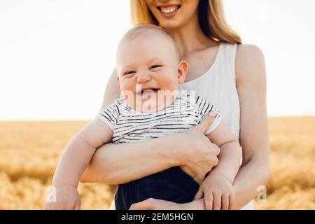 Happy beautiful mother with her baby on the golden wheat field, family on the grain field, mom hugs her little boy Stock Photo
