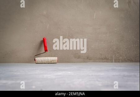 Paint roller in empty room on cement floor. Grunge interior background. Stock Photo