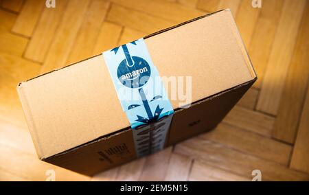 Paris, France - Nov 16, 2018: POV male hand holding looking at the new freshly delivered Amazon Prime cardboard parcel on the wooden parquet floor Stock Photo