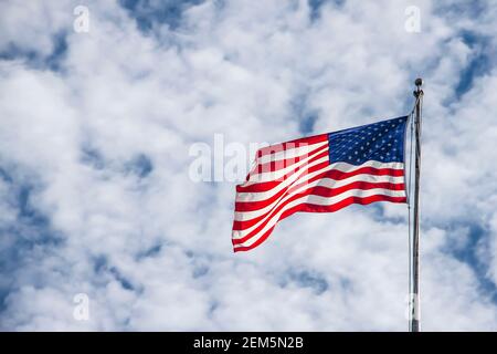 Waving American flag on flagpole against dramatic puffy cloud sky - Room for copy. Stock Photo