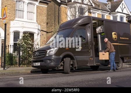 UPS delivery man offloading parcels from van on road side near residential houses Stock Photo