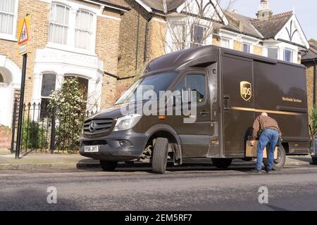 UPS delivery man offloading parcels from van on road side near residential houses Stock Photo