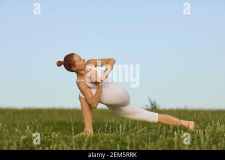 Slim female doing Revolved Crescent Lunge while practising yoga on green summer meadow Stock Photo