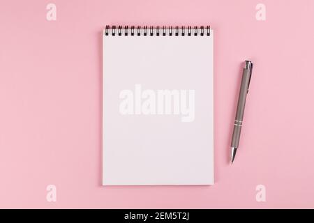 A notebook with a blank page and a ballpoint pen lie on a pink background Stock Photo