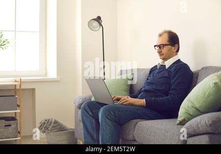 Mature remote worker using his laptop while sitting on comfortable couch at home Stock Photo