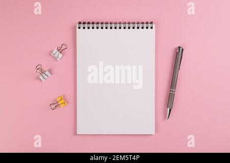 A notebook with a blank page, a ballpoint pen and multi-colored clips for paper lie on a pink background Stock Photo